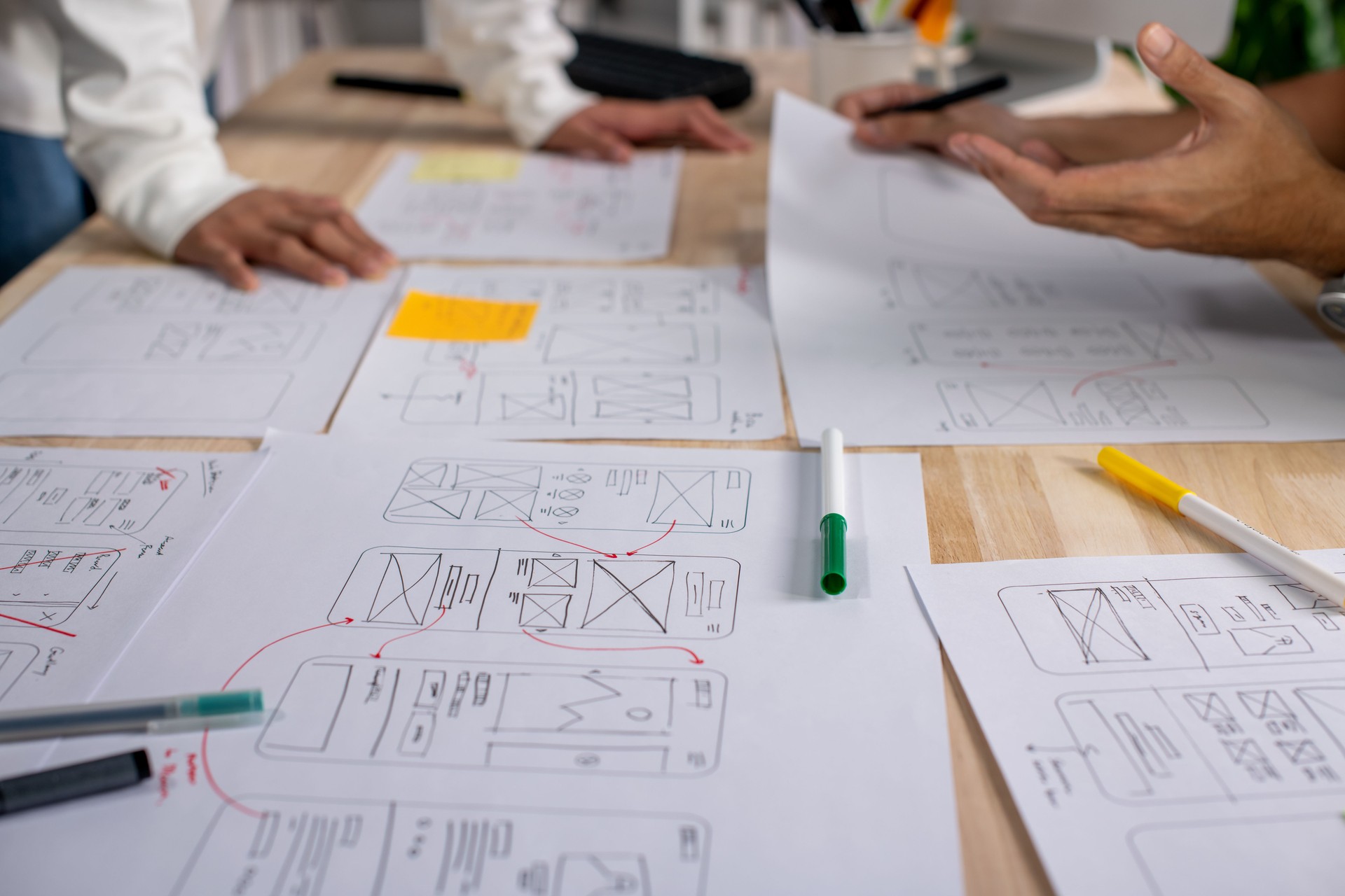 UX UI designers discussing and brainstorming on wireframes for a website and mobile app prototype, surrounded by sketches of user flow and design tools, in the concept of website and mobile application design concept.